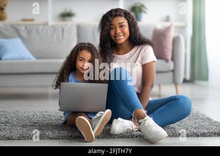 Fernschulungskonzept. Glückliche schwarze Mutter und ihre niedliche kleine Tochter beobachten Online-Unterricht auf Laptop zu Hause Stockfoto