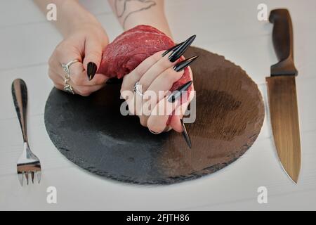 Junge weibliche Hände mit langen Nägeln halten rohes Fleisch. Stockfoto