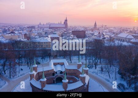 Barbikan und die Krakauer Altstadt im Winter. Schnee auf den Dächern im Winter Krakau Polen bei Sonnenuntergang. Mittelalterliche Festung Barbacan, Royal Road und Stadtzentrum. Stockfoto