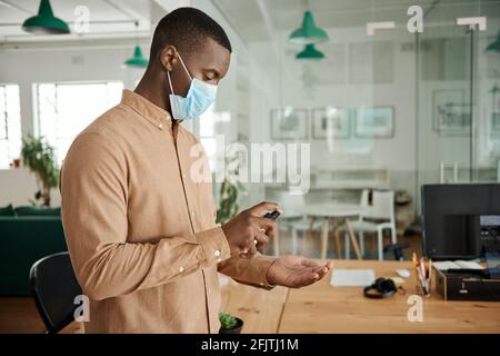 Afrikanischer Geschäftsmann, der eine Maske mit Handdesinfektionsmittel bei der Arbeit trägt Stockfoto