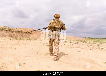 Spezialwehrsoldat in Tarnung mit Gewehr geht durch die Wüste Stockfoto