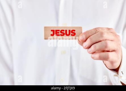 Männliche Hand hält einen Holzblock mit dem Wort Jesus. Heilige Jesus Christus Religion Konzept. Stockfoto