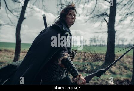 Die Frau im Bild des mittelalterlichen Kriegerbogens geht durch den Wald mit Bogen in der Hand und Pfeilen im Köcher. Stockfoto