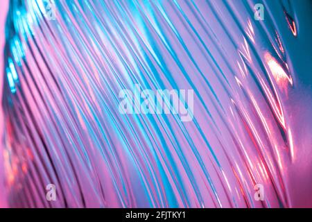 Abstrakter Glashintergrund. Textur aus gewelltem Glas, beleuchtet mit mehrfarbigem Licht. Rosa und blaue Flecken. Nahaufnahme. Fackeln auf Glas Stockfoto