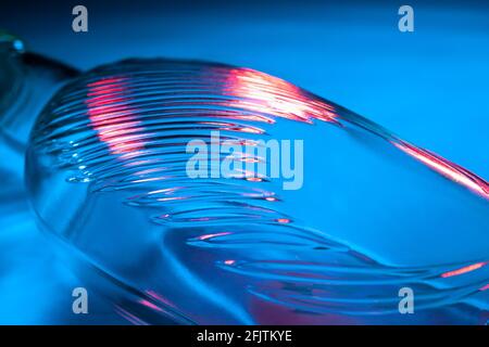 Abstrakte Glasflasche Hintergrund. Textur aus gewelltem Glas, beleuchtet mit mehrfarbigem Licht. Rosa und blaue Flecken. Nahaufnahme. Fackeln auf Glas Stockfoto