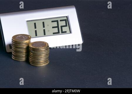 Digitale Tischuhr mit Münzen an der Seite auf schwarz Hintergrund Stockfoto