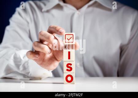 Überprüfung der ISO-Normen, Zertifizierung der Qualitätskontrolle. Geschäftsmann legt einen Würfel mit einem Häkchen auf die abgestuften Holzwürfel mit dem Wor Stockfoto