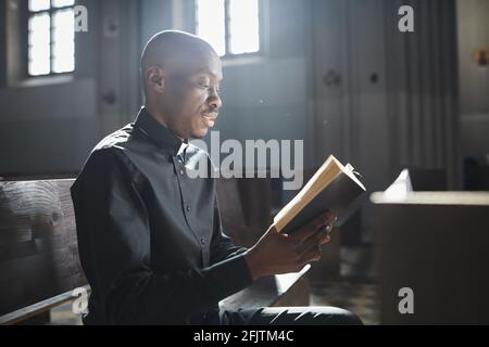 Afrikanischer Priester im Kragen, der die Bibel liest und davor steht Des Altars in der Kirche Stockfoto