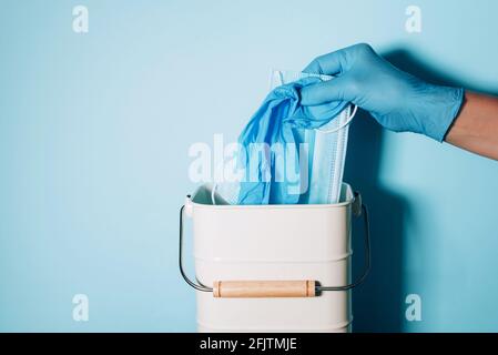 Hand in medizinischen Handschuhen wirft medizinische Maske in Mülleimer auf blauem Hintergrund. Quarantäne beendet. Covid 19. Konzept des Coronavirus-Endes. Banner mit Kopie Stockfoto