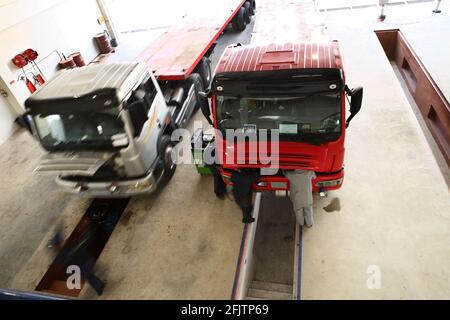 Eine Gruppe von Mechanikern arbeitet an 2 Lkw, die in einer Reparaturwerkstatt für schwere Lkw geparkt sind. Stockfoto