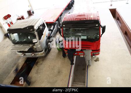 Eine Gruppe von Mechanikern arbeitet an 2 Lkw, die in einer Reparaturwerkstatt für schwere Lkw geparkt sind. Stockfoto