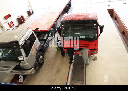 Eine Gruppe von Mechanikern arbeitet an 2 Lkw, die in einer Reparaturwerkstatt für schwere Lkw geparkt sind. Stockfoto