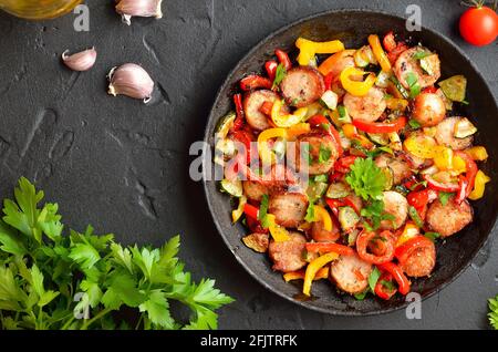 Scheiben von gebratenem Gemüse mit Würstchen und Gewürzen in der Pfanne. Ansicht von oben, flach Stockfoto