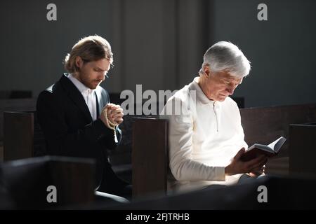 Männer sitzen auf der Bank und beten in der Kirche Während der Masse Stockfoto