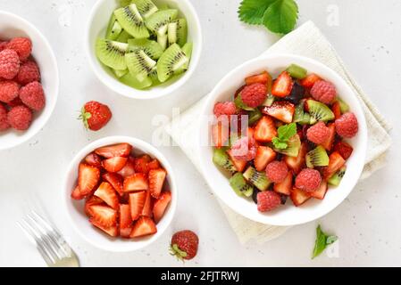 Gesundes Frühstück mit Obstsalat aus Erdbeere, Kiwi und Himbeere auf hellem Steingrund. Draufsicht, flach liegend Stockfoto