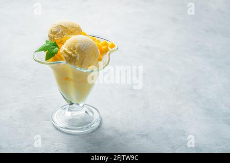 Kugeln aus cremigem Mango-Eis in einem transparenten Glas auf grauem Hintergrund. Seitenansicht, Kopierbereich. Stockfoto