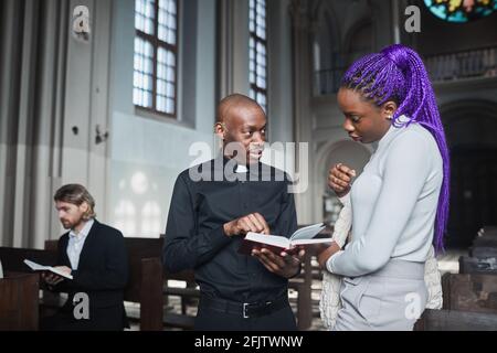 Junge afrikanische Frau diskutiert Bibel zusammen mit Priester, während sie Steht in der Kirche Stockfoto
