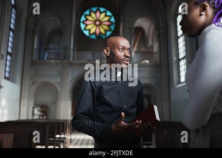 Afrikanischer junger Priester, der mit der Frau spricht und die Teile diskutiert Der Bibel, die in der Kirche steht Stockfoto