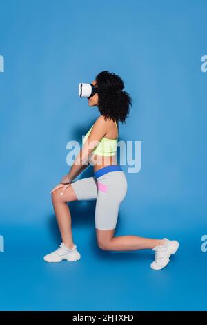 Lächelnde afroamerikanische Frau in voller Länge im vr-Headset Training auf Blau Stockfoto