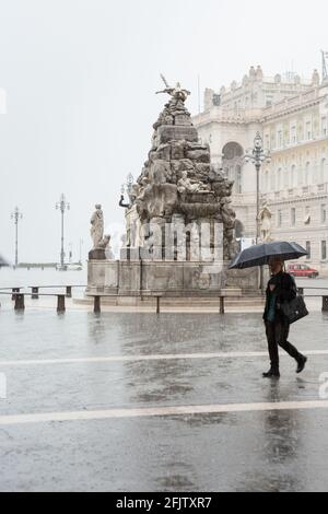 Eine Person mit einem Regenschirm geht bei starkem Regen am Brunnen der vier Kontinente (Fontana dei Quattro Continenti), Piazza Unità d'Italia, Triest, vorbei Stockfoto