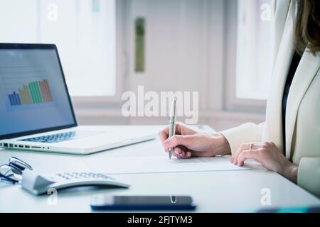 Eine kurze Aufnahme einer nicht erkennbaren Finanzkauffrau, die den Vertrag unterschrieb, während sie am Schreibtisch saß und arbeitete. Stockfoto