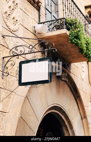 Schönes blank Schild in einem geschmiedeten Metallrahmen hängt an Eine Steinmauer eines Gebäudes vor einem Hintergrund von Balkon und Grün Stockfoto