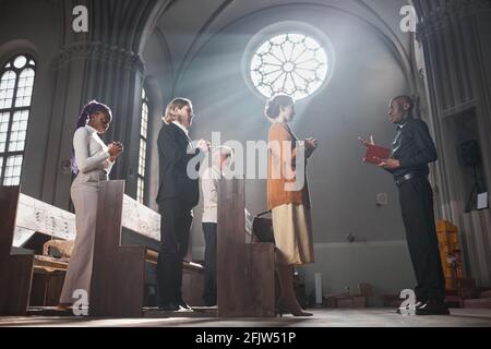 Gruppe von Menschen stehen und beten während der Messe zusammen mit Priester in der Kirche Stockfoto
