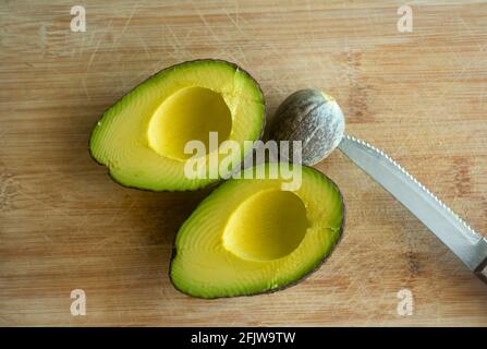 Nahaufnahme einer halbiert geschnittenen Avocado auf einem rustikalen Holzsockel und ein Messer in den Stein geklebt Die Früchte Stockfoto