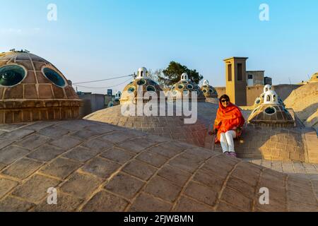 Lady mit orangefarbenem Schal sitzt auf dem Dach mit mehreren Kuppeln des Sultan Amir Ahmad (oder Qasemi) Badehaus. Kashan, Iran. Stockfoto