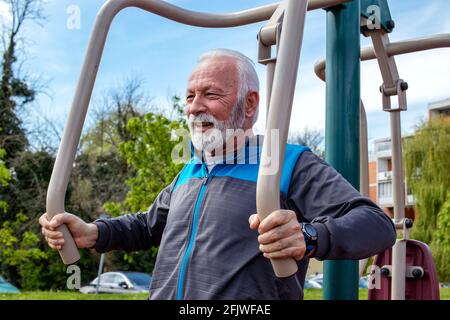 Ein älterer graubärtiger Mann übt im Freien an den öffentlichen Fitnessgeräten. Stockfoto