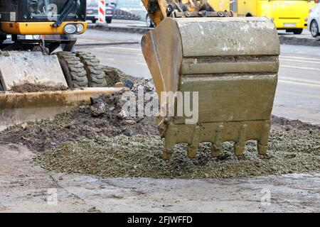 Ein Straßenbaggereimer gießt Betonkies auf einer Baustelle. Nahaufnahme. Stockfoto