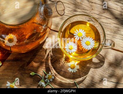 Glas Kräutertee und Kamillenblüten in der Nähe der Teekanne. Nahaufnahme. Stockfoto