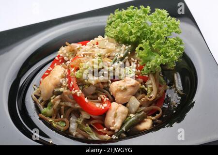 Chinesische Nudeln mit Hühnchen und Gemüse auf einem schwarzen Teller. Stockfoto