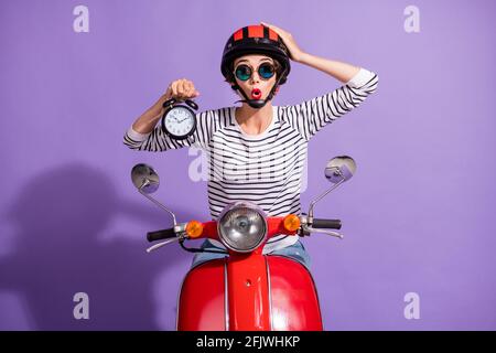 Portrait Foto von geschockten Mädchen Vorführung Uhr in Helm Sonnenglas Berühren Kopf Frist spät isoliert auf hellviolettem Hintergrund Stockfoto