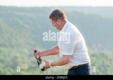 Ein Mann öffnet eine Flasche Sekt auf dem Hintergrund des Waldes Stockfoto