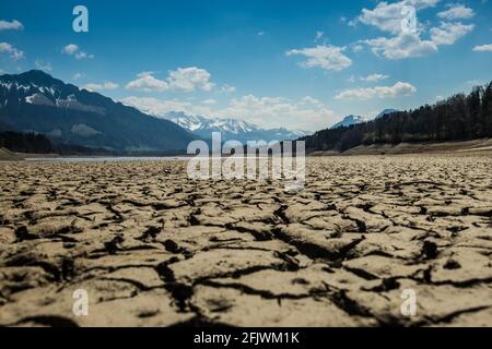 Landschaftsaufnahme des ausgetrockneten "Sees von Gruyere", mit verschneiten Alpen im Hintergrund, aufgenommen in Corbieres, Freiburg, Schweiz Stockfoto