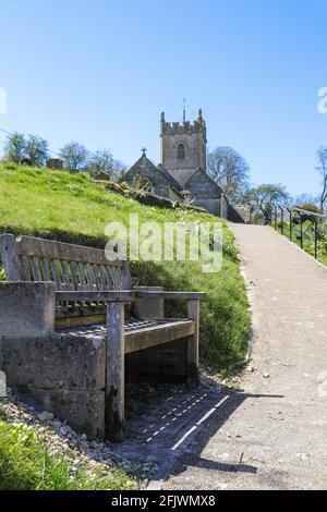 Eine Sitzbank aus Holz als Ruheplatz auf dem Weg zur St. Oswald-Kirche im Cotswold-Dorf Compton Abdale in Gloucestershire, Großbritannien Stockfoto