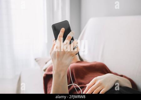 Frau Hand mit einem schwarzen Handy macht einen Videoanruf Mit weißen Kopfhörern Stockfoto