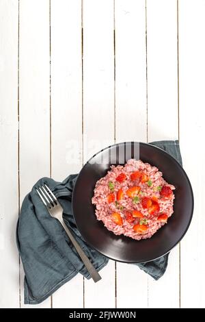 Risotto mit Erdbeerfrüchten serviert in einem schwarzen Gericht auf einem weißen Holztisch. Flach liegend mit Kopierraum. Italienische Gourmetküche. Selektiver Fokus. Stockfoto