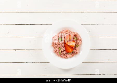 Risotto mit Erdbeerfrüchten serviert in einem weißen Gericht auf einem Holztisch. Flach liegend mit Kopierraum. Italienische Gourmetküche. Selektiver Fokus. Stockfoto