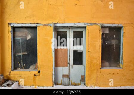 Alte verlassene venezianische Hausfassade mit ockerfarbener Stuckwand und verwitterter Holztür und Fensterläden in Nafplio, Argolis Peloponnes, Griechenland. Stockfoto