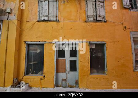 Alte verlassene venezianische Hausfassade mit ockerfarbener Stuckwand und verwitterter Holztür und Fensterläden in Nafplio, Argolis Peloponnes, Griechenland. Stockfoto