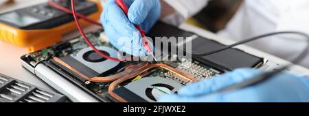 Professionelle Werkstatt hält roten Tester in Gummihandschuhen über Laptop Nahaufnahme Stockfoto