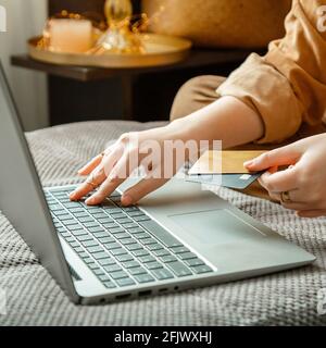 Weibliche Hände mit Karten Laptop. Käufer kauft Waren oder Dienstleistungen online im Wohnzimmer. Shopper kauft online mit Laptop und Guthaben ein Stockfoto