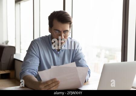 Junge männliche Angestellte arbeiten am Arbeitsplatz mit Papierkram Stockfoto
