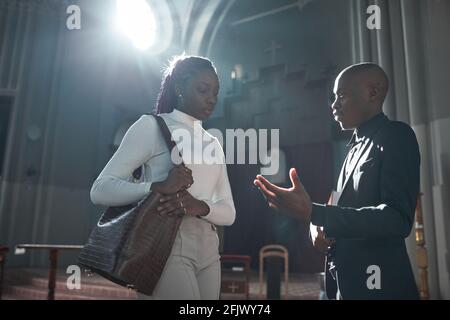 Afrikanische Frau im Gespräch mit dem Priester nach der Zeremonie in der Kirche Stockfoto