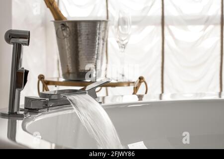 Führen Sie das Wasser aus dem Wasserhahn eines breiten Badezimmers in einen aus Heißer Whirlpool mit Eiskübel und Sektglas auf dem Zurück Stockfoto