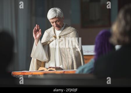 Leitender Priester beim Lesen der Bibel für Menschen während der Zeremonie in Die Kirche Stockfoto