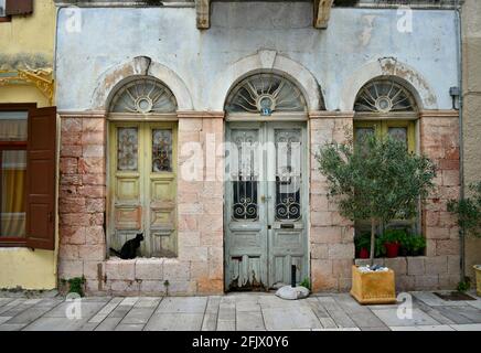 Alte verlassene Hausfassade mit verwitterter Steinmauer und gewölbter Tür und Fenstern mit handgefertigten Eisengittern in Nafplio Peloponnes, Griechenland. Stockfoto