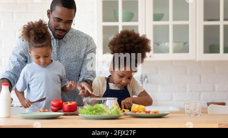 Glückliche afroamerikanische Geschwisterkinder helfen dem Vater, das Abendessen zuzubereiten Stockfoto